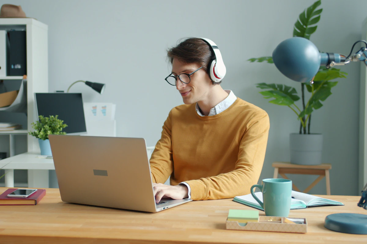 A person wearing over-ear headphones while working on a laptop at a desk.
